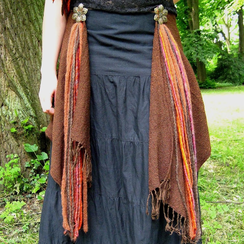 May include: A brown skirt with long fringe and two decorative metal flower brooches. The skirt is layered and has a black top underneath.