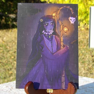 May include: An illustration of a figure in a purple dress, holding a staff with lanterns and a skull. The artwork has a dark, rainy atmosphere. The figure has long black hair and a floral headpiece. The image is displayed on a wooden easel.