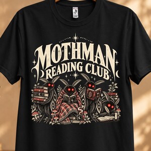 May include: A black short-sleeve t-shirt featuring a graphic print with the text "MOTHMAN READING CLUB" in a stylized font. The illustration depicts four moth-like creatures with glowing red eyes reading books, surrounded by small mushrooms.