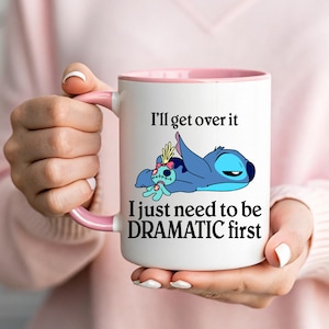 May include: White ceramic mug with a pink interior and handle. The mug features a blue cartoon character with the text "I'll get over it, I just need to be DRAMATIC first."