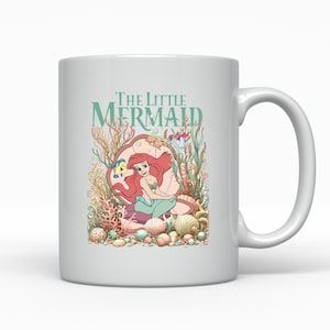 A white ceramic mug featuring an illustration of the mermaid character from the Disney film "The Little Mermaid".