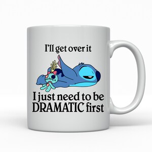 A white ceramic mug with a cartoon image of a blue character and text that reads "I'll get over it, I just need to be DRAMATIC first".
