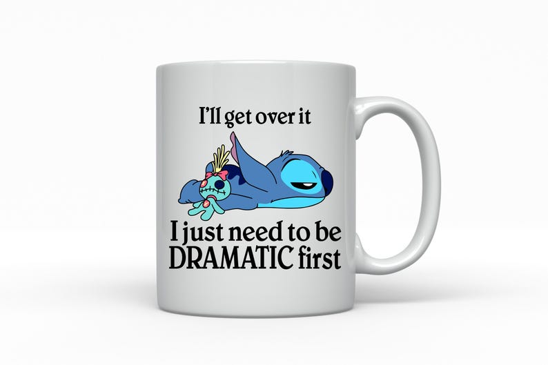 A white ceramic mug with a cartoon image of a blue character and text that reads "I'll get over it, I just need to be DRAMATIC first".