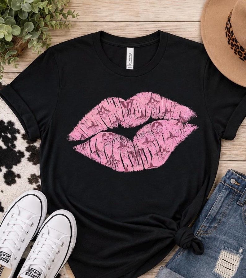 K&ouml;nnte beinhalten: Ein schwarzes Kurzarm-T-Shirt mit einer gro&szlig;en, zentralen Grafik von rosa Lippen. Die Lippen sind mit einem sich wiederholenden Muster aus kleinen, dunkelrosa Blumen- und Geometriesymbolen gef&uuml;llt. Das T-Shirt hat einen Rundhalsausschnitt.