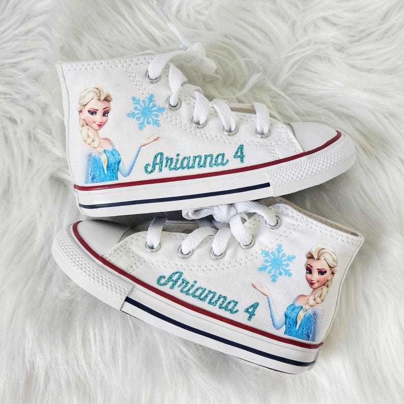 May include: White high-top canvas shoes with a blue and white image of Elsa from Frozen, a snowflake, and the name "Arianna 4" in glitter.