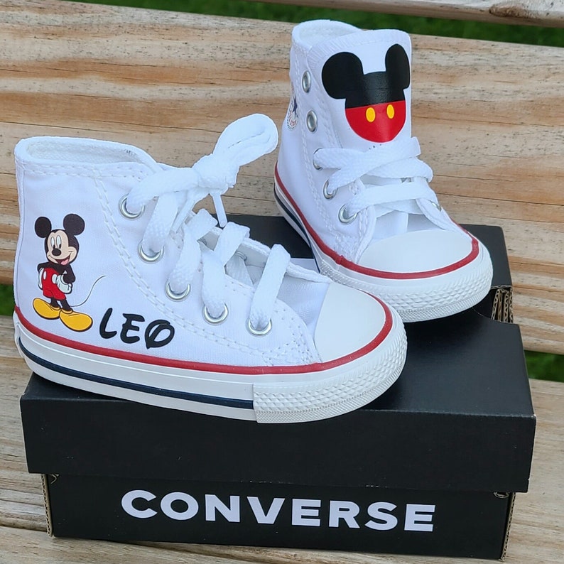 May include: White high-top sneakers with Mickey Mouse graphics. One shoe features a full Mickey Mouse image, the other has a Mickey Mouse head. The name "LEO" is printed on one shoe. The shoes have white laces and red and blue trim.