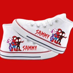 Puede incluir: Zapatillas blancas de lona de ca&ntilde;a alta con un dise&ntilde;o de dibujos animados rojo, negro y morado de personajes de Spider-Man. Las zapatillas est&aacute;n personalizadas con el nombre "SAMMY" en ambos lados.