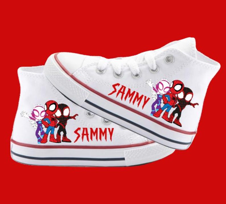 Puede incluir: Zapatillas blancas de lona de ca&ntilde;a alta con un dise&ntilde;o de dibujos animados rojo, negro y morado de personajes de Spider-Man. Las zapatillas est&aacute;n personalizadas con el nombre "SAMMY" en ambos lados.