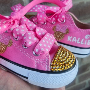 May include: Pink and white polka dot canvas shoes with gold glitter Mickey Mouse ears and rhinestones. The shoes are personalized with the name "Kallie".