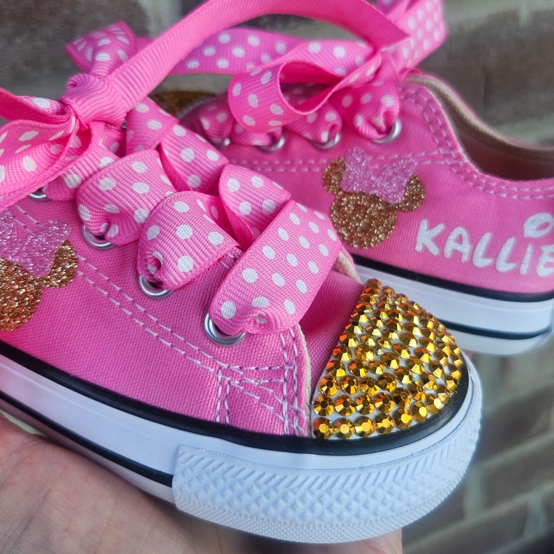 May include: Pink and white polka dot canvas shoes with gold glitter Mickey Mouse ears and rhinestones. The shoes are personalized with the name "Kallie".