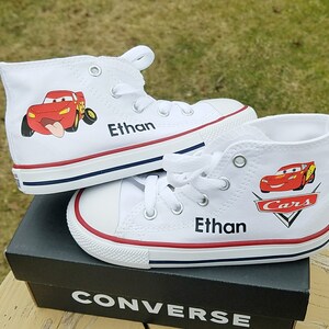 K&ouml;nnte beinhalten: Wei&szlig;e Converse-Sneaker mit hohem Schaft, mit einem roten Lightning McQueen Cars-Charakterdesign und dem Namen "Ethan" darauf.