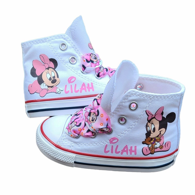 May include: White high-top canvas shoes with pink Minnie Mouse designs and the name "Lilah" written on the side. The shoes have a pink ribbon bow with Minnie Mouse designs.