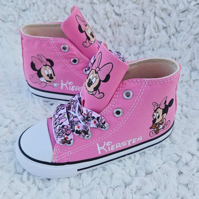May include: Pink high-top canvas sneakers with white laces and a white rubber sole. The shoes feature a Minnie Mouse design with a pink bow and the name "Kiersten" written on the side.