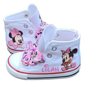 May include: White high-top canvas shoes with a pink bow and Minnie Mouse design. The shoes are personalized with the name "Lilah".