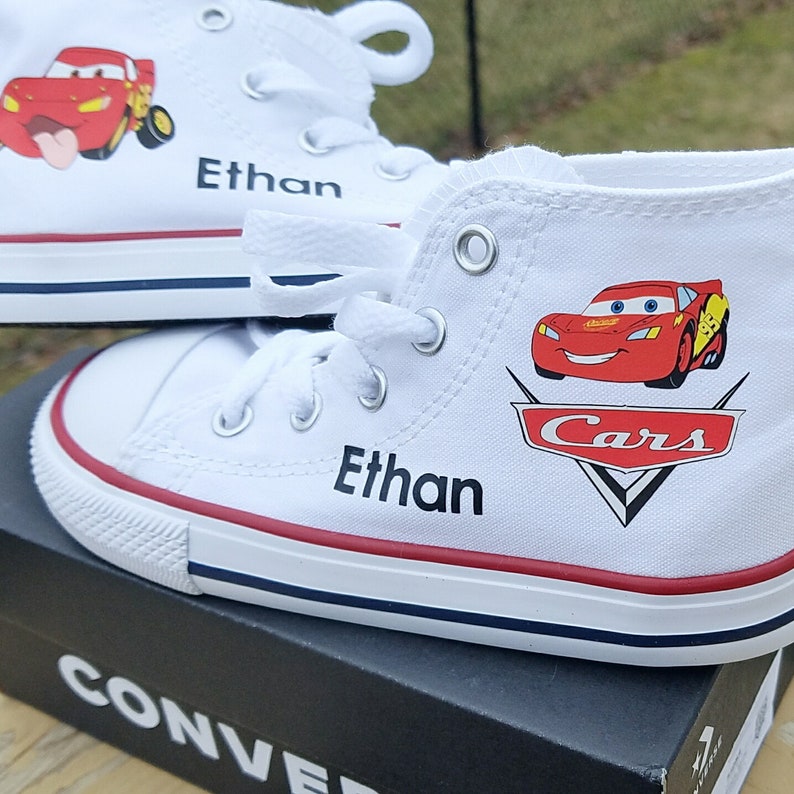 K&ouml;nnte beinhalten: Wei&szlig;e Canvas-High-Top-Sneaker mit einem roten und schwarzen Cars-Design mit Lightning McQueen. Die Schuhe sind mit dem Namen "Ethan" personalisiert.