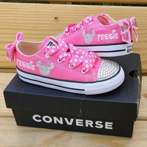 May include: Pink Converse sneakers with white polka dot ribbon laces and a sparkly Minnie Mouse design. The shoes are personalized with the name "Jessie" in white lettering.