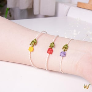 May include: Three handmade bracelets with a white cord and a colorful tulip design. Each bracelet features a different colored tulip: yellow, red, and purple. The tulip petals are intricately crocheted with green leaves.