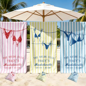 May include: Three striped beach towels in pink, yellow, and blue, each with a bikini illustration and the text "THE BRIDE CLUB TRACY'S Bachelorette CAPE COD AUG 2026". Small matching bags are at the base of each towel.