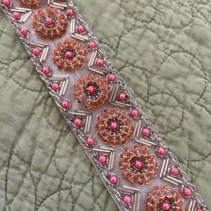 May include: A white trim with pink and orange beads and sequins in a floral pattern.
