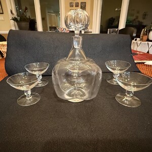 Puede incluir: Una jarra de cristal transparente con cuerpo bulboso y tapón decorativo, acompañada de cuatro copas de tallo a juego. El juego de cristalería es para servir bebidas y tiene un diseño clásico y elegante.