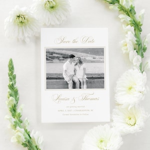 May include: A wedding announcement card with a black and white photo of a couple, surrounded by white flowers and greenery. The card reads "Save the Date" and includes the names Louisa & Thomas, the wedding date, and location.