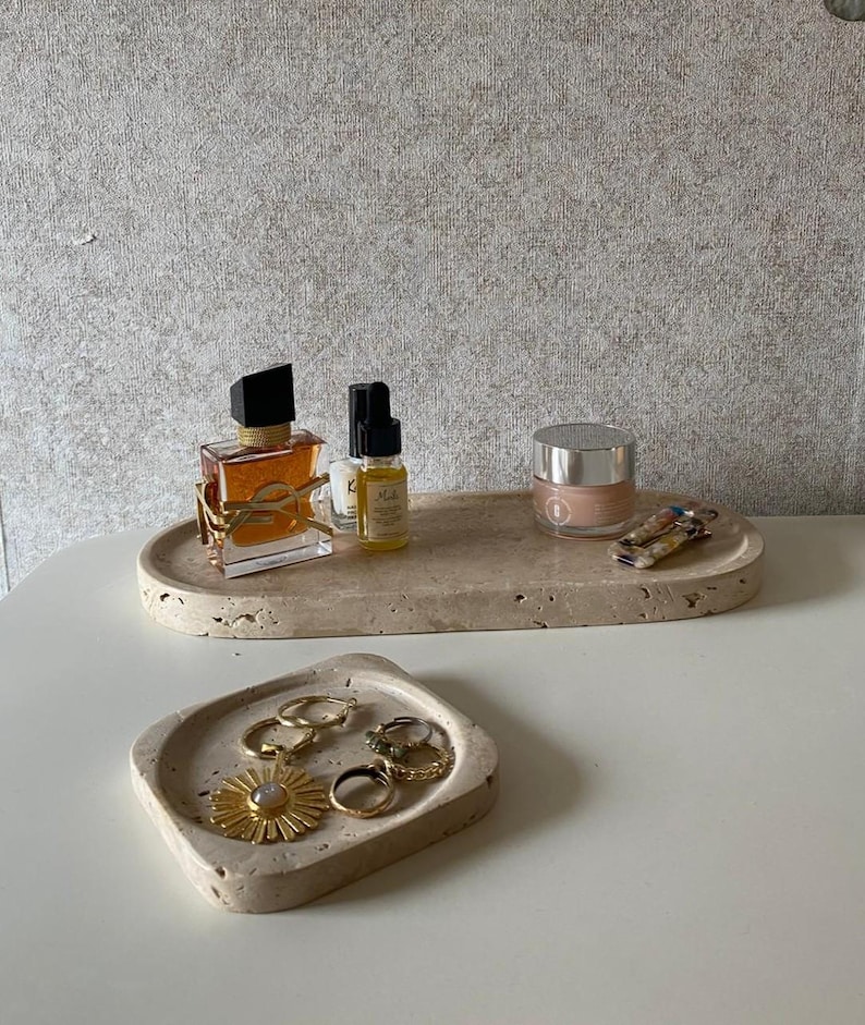 Pu&ograve; includere: Due vassoi in pietra di travertino beige con una consistenza porosa. Il vassoio ovale pi&ugrave; grande contiene un flacone di profumo quadrato con un logo dorato, due piccoli flaconi contagocce, un barattolo di crema rotondo e una molletta per capelli. Il vassoio quadrato pi&ugrave; piccolo contiene gioielli dorati.