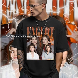 May include: Black t-shirt with the word "ENGLOT" in orange block letters. The shirt features a collage of four women in the centre. The background has a blurred image of women and lightning bolt graphics.