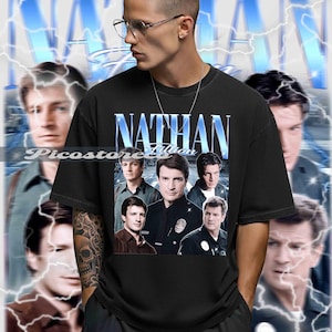 May include: Black t-shirt with a blue and white design featuring the text "NATHAN Fillion" and a collage of images. The shirt has a vintage aesthetic and a crew neck.