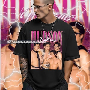 May include: Black t-shirt featuring a vintage-style graphic of the band "Hudson Williams." The design includes a group photo of the band members and the band's name in a pink, retro font. The background has a pink and white lightning bolt design.