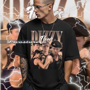 以下が含まれることがあります： 黒いTシャツ。軍服姿の人々のヴィンテージスタイルのグラフィックと「DIZZY Flores」の文字。背景には稲妻のグラフィックが描かれています。