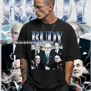 Könnte beinhalten: Schwarzes T-Shirt mit einem Grafikdesign von Rudy Giuliani und dem Schriftzug "RUDY" in metallischer Schrift. Die Person, die das T-Shirt trägt, hat ein Tattoo auf dem Arm. Der Hintergrund hat ein Blitzmuster.