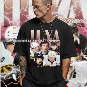May include: Black t-shirt featuring a collage of hockey players with the name "Ilya Rozanov" in a vintage style. The design includes a faded background with lightning bolt graphics, creating a retro aesthetic.