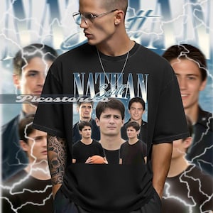 May include: Black t-shirt featuring a collage of images and the name "Nathan Scott" in a stylized font. The design includes multiple images of a person, with a basketball in one image. The background has a blue and white lightning design.