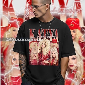 May include: Black t-shirt featuring a group of people in red outfits and the name "Katya Zamolodchikova" in red and white text. The background has a red and white design with lightning bolts.