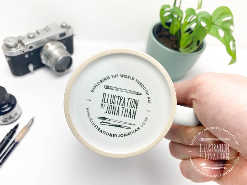 Puede incluir: Taza de cer&aacute;mica blanca con una ilustraci&oacute;n en blanco y negro de l&aacute;pices y pinceles. El texto en la taza dice "Explorar el mundo a trav&eacute;s del arte. Ilustraci&oacute;n de Jonathan. www.illustrationbyjonathan.co.uk"