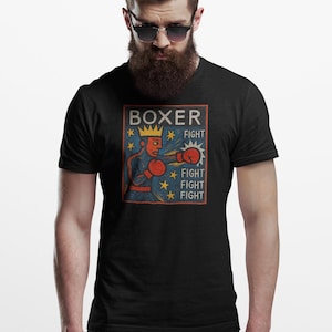 Può includere: T-shirt nera con grafica a tema pugilato in stile vintage. Il design presenta un pugile con una corona che tira un pugno, con la scritta "BOXER" e la parola "FIGHT" ripetuta tre volte, più stelle.