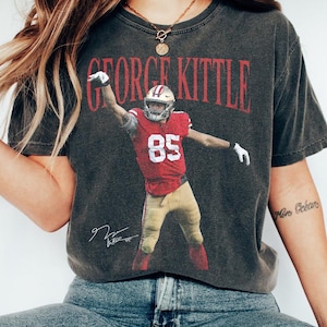 Könnte beinhalten: Ein anthrazitfarbenes Kurzarm-T-Shirt mit einer Grafik von George Kittle in einem roten San Francisco 49ers-Trikot mit der Nummer 85. Der Name GEORGE KITTLE ist in Rot über dem Spieler gedruckt und eine weiße Unterschrift befindet sich unten.