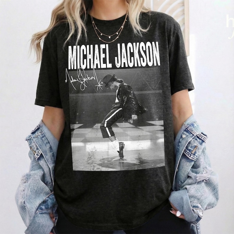 May include: Charcoal grey t-shirt with a monochrome image of Michael Jackson performing. The shirt displays the text "MICHAEL JACKSON" in white, with his signature above the image. A classic music-themed tee.