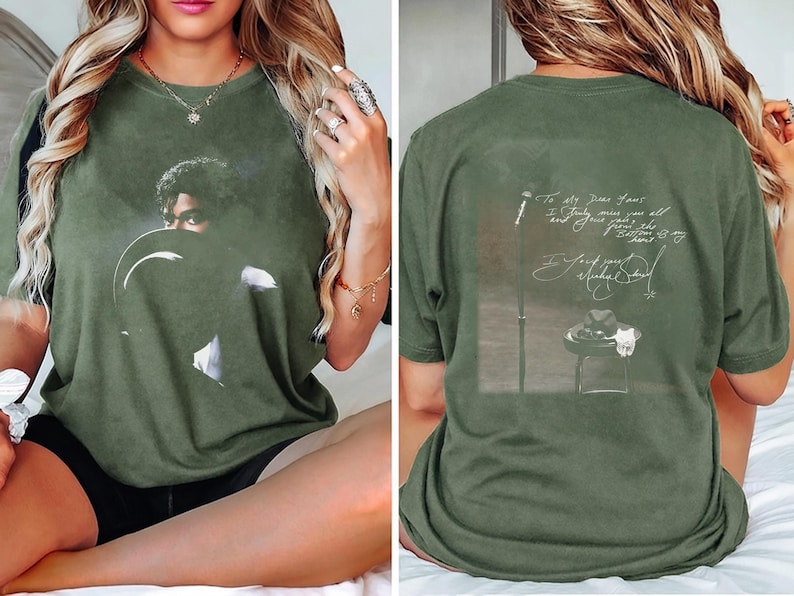 May include: Olive green t-shirt featuring a portrait of a person with a hat on the front. The back of the shirt has a graphic with text and a signature. The shirt is a relaxed fit.
