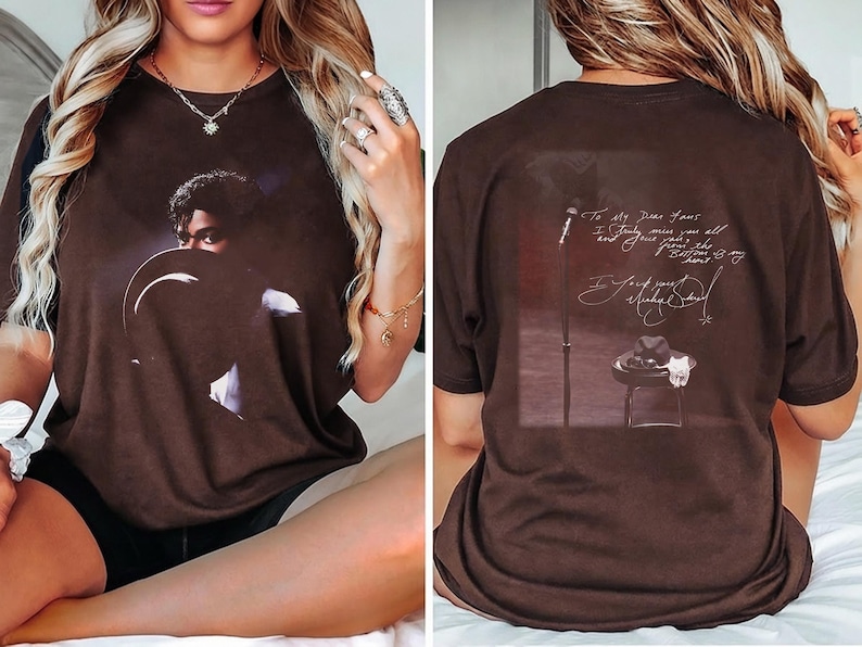 May include: Brown t-shirt featuring a portrait of a musician. The front of the shirt displays a close-up image of the musician. The back of the shirt has a graphic of a microphone, a hat, and text that reads "To my dear fans..."