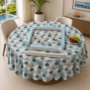 May include: A round tablecloth with a blue and white fan-shaped pattern covering a table set with a Mahjong game. The game features rectangular tiles with Chinese characters and symbols arranged in rows and scattered across the patterned surface.