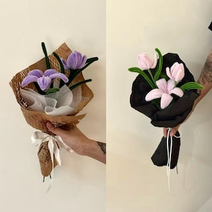 May include: Two bouquets of handmade flowers. One bouquet features purple flowers wrapped in brown paper with a white ribbon. The other bouquet has pink flowers wrapped in black paper with white string. Both bouquets have green stems.
