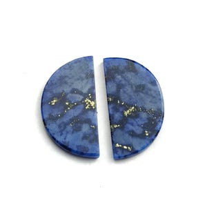 Könnte beinhalten: Zwei polierte, halbkreisförmige Lapislazuli-Steine. Die Steine haben eine tiefblaue Farbe mit goldenen Flocken. Die Steine sind in Halbmondform geschnitten und vor einem weißen Hintergrund platziert.