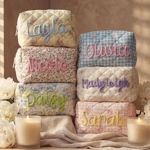 May include: A stack of personalized quilted cosmetic bags in various floral and gingham patterns. Each bag features a name embroidered in a contrasting color: Layla, Nicole, Daisy, Olivia, Madyleigh, and Sarah. Two lit candles and flowers are in the foreground.