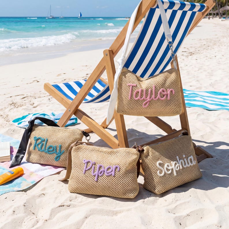 Puede incluir: Cuatro bolsos de playa de paja tejida con nombres personalizados: "Taylor" en rosa, "Riley" en turquesa, "Piper" en lavanda y "Sophia" en blanco. Los bolsos son rectangulares y est&aacute;n sobre una playa de arena, cerca de una tumbona.