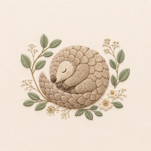 May include: An embroidery design featuring a curled-up pangolin with textured tan scales and a closed eye. The pangolin is surrounded by a delicate wreath of embroidered green leaves, small white flowers, and thin brown stems on a cream fabric.