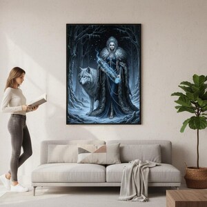 May include: A framed art print depicting a fantasy scene with a woman in a dark gown and a wolf in a snowy forest. The woman holds a glowing blue object. The artwork is in a black frame and hangs on a white wall.