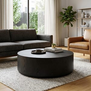 May include: A large, round, black wooden coffee table with a visible wood grain texture. The table features a low-profile, cylindrical base and a flat top surface. It is positioned centrally, serving as a focal point for the surrounding furniture.