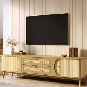 May include: A light wood-tone TV stand with two drawers and two cabinet doors. The doors have a vertical ribbed design and the drawers have a woven cane design. The stand is set against a light wood-paneled wall.