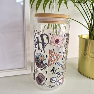 May include: A clear glass tumbler with a bamboo lid and a glass straw. The tumbler is decorated with colourful Harry Potter-themed graphics, including the HP logo, a letter, and the words "Always" and "Muggles".